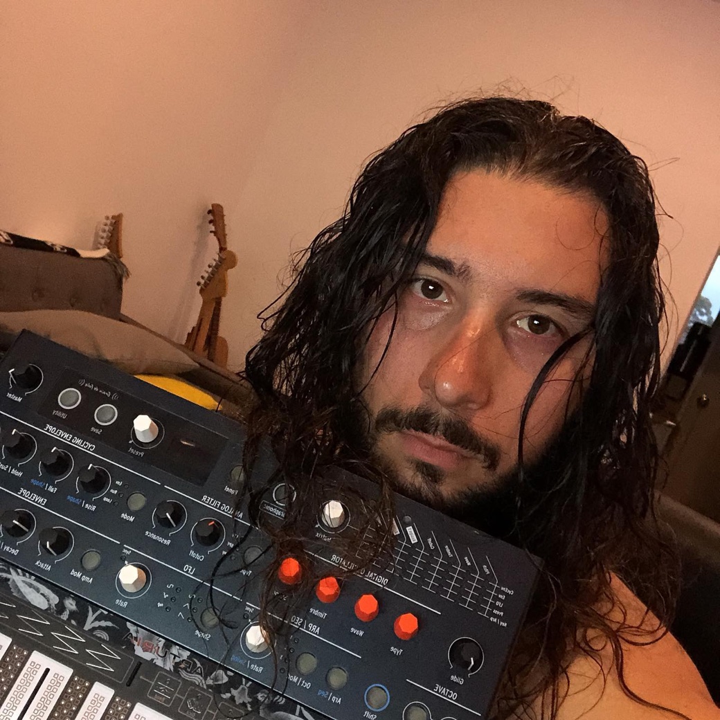 Mickey Nox mit einem Hardware-Synthesizer, im Hintergrund Gitarren an der Wand